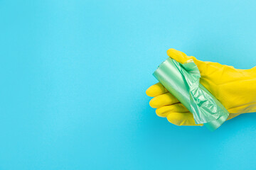 A hand in a yellow glove holds a plastic disposable trash bag on a blue background. place with copy...
