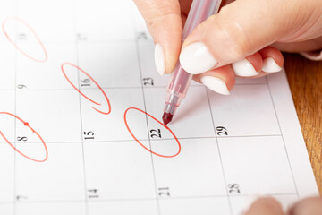 close up on employee woman hand using red pen to writing schedule on calendar 2022 to make an...