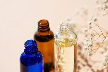 Open amber, blue and transparent bottles without cap with serum or essential oil with white flowers. Beige background with daylight and beautiful shadows. Beauty concept for face and body care