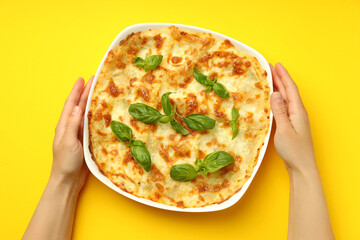 Female hands and Lasagna on yellow background