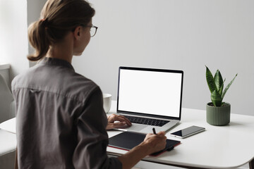 Young woman using laptop computer with white mockup screen at home. Business woman working in office. Freelance, student lifestyle, e-learning, web site, technology and online meeting concept