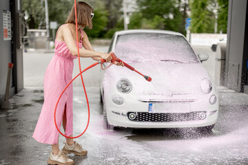 Woman in pink dress washing her tiny car with nano foam at car wash