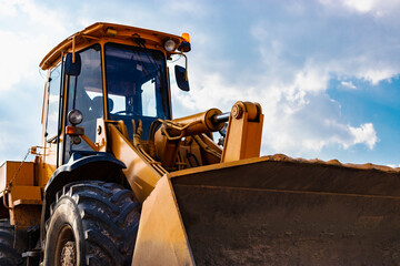 Bulldozer or loader moves the earth at the construction site against the blue sky. An earthmoving...