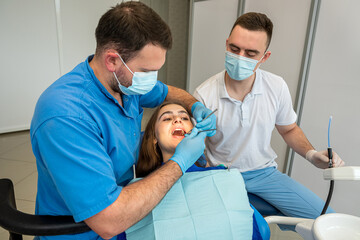 Pretty female patient sitting in armchair while doctor with assistant examining her teeth