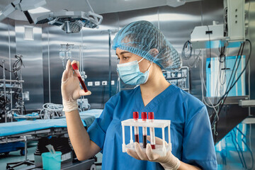 Fototapeta young nurse in protective uniform glove hat and mask looks at blood samples in operating obraz