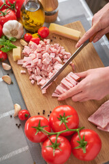 woman's hands slicing pancetta ham bacon on wooden cutting board at domestic kitchen