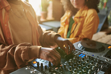 Hands of African American guy in sweatshirt adjusting dj controller while creating new music for...