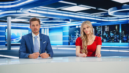 TV Live News Program: Two Presenters Reporting, Talking, Discuss Daily Events, Friendly Chat. Television Cable Channel Diverse Team of Male and Female Anchors Talk. Newsroom Studio Concept
