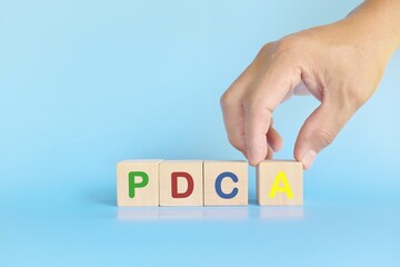 PDCA or Plan Do Check Act cycle method concept. Hand putting action wooden blocks in blue background with copy space.