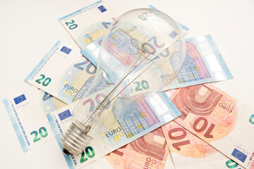 Obraz na płótnie Canvas Light bulb on euro banknotes. Cost of electricity and expensive energy concepts. Increasing consumption, energy crisis. Inflation. Price level are getting more expensive annually.