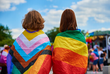 Cheerful women couple under LGBTQ rainbow flags on pride parade. Tolerance, diversity and gender...
