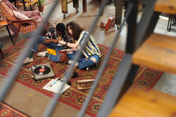 Young couple sitting on red carpet on the floor of living room and discussing images on screen of...