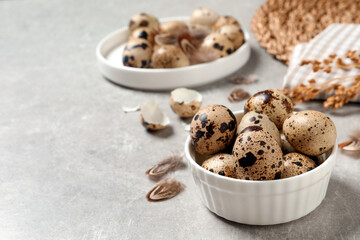 Fresh quail eggs in bowl on light grey table. Space for text