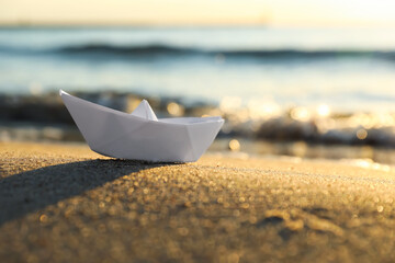 Fototapeta White paper boat on sand near sea at sunset, closeup. Space for text obraz