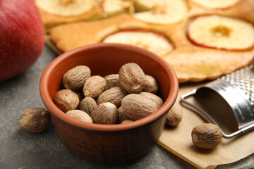 Nutmeg seeds, grater and apple pie on grey table, closeup