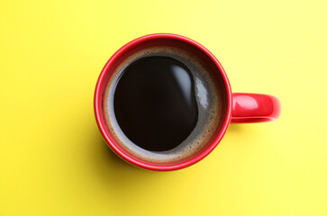 Fresh aromatic coffee in red mug on yellow background, top view