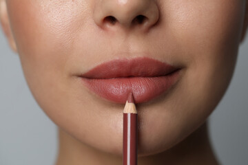 Naklejka premium Young woman applying beautiful nude lip pencil on grey background, closeup