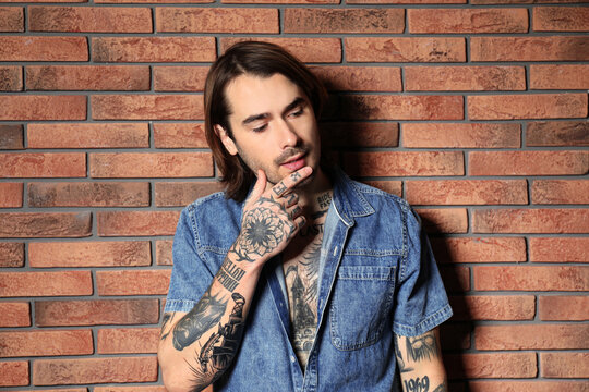 Young man with tattoos on body near brick wall