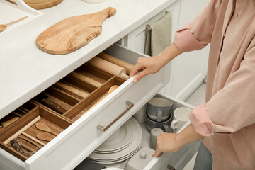 Woman opening drawers of kitchen cabinet with different dishware and utensils, closeup - obrazy, fototapety, plakaty