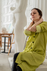 Tired female artist in art studio sits with her hands on her neck