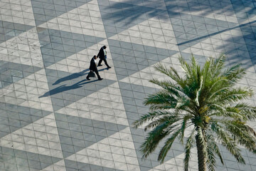 Two people in distant silhouette cross a city plaza in Dubai, UAE.