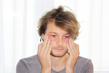 Anti-aging eye therapy. young man taking care of his undereye wrinkles applying facial mask. Dark Circles.Eye patches..