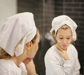 woman looking in the mirror in the bathroom and taking care of her skin.Applying the cream..Magic anti-aging cream.
