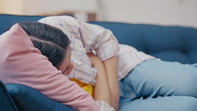 Asian woman suffering from abdominal pain while lying on sofa, period cramps