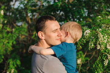 Fototapeta premium Father's Day. Father and son are playing and hugging on a green background of foliage and acacia. Happy family.