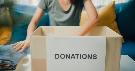 Happy young Asia teenage girl volunteer packing clothes product into donation cardboard boxes while...