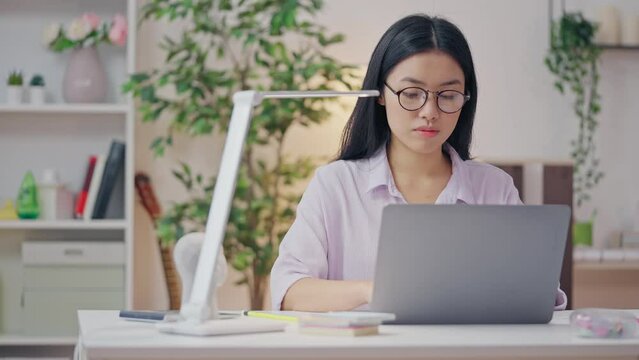 Young Asian woman working from home during lockdown, typing on laptop, app