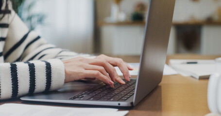 Freelance Asia lady casual wear using laptop online in kitchen at home office. Working from house, remotely work, distance education, social distancing, quarantine for coronavirus. Close up shot.