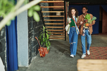 Happy young intercultural couple in stylish casualwear moving along living room of loft apartment...