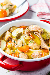 Chicken stew with potatoes and carrots in red saucepan. Chicken soup with vegetables and herbs. Comfort food recipe.