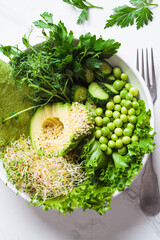 Green buddha bowl with avocado, peas, cucumber, sprouts and tortilla, close-up. Vegan healthy salad in white bowl.