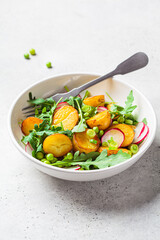 Summer potato and pea salad with arugula and radish in a white bowl. Vegan recipe.