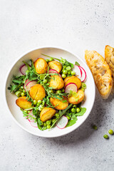Summer potato and pea salad with arugula and radish in white bowl. Vegan recipe.