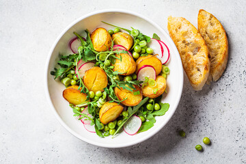 Summer potato and pea salad with arugula and radish in white bowl. Vegan recipe.
