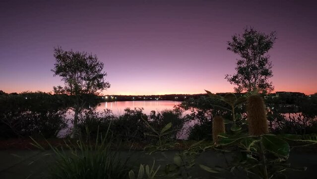 The sun goes down over a lakeside suburb. A busy footpath illuminates over time.