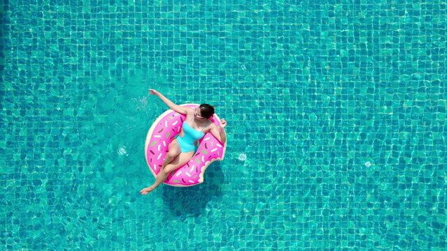 Top view of young asian woman in swimsuit on the pink donut lilo in the swimming pool.
