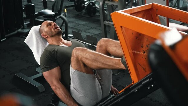 Extremly tired bald well-built man lying on a bench exercising on a leg press. Indoor shot at a well-equipped gym. High quality 4k footage
