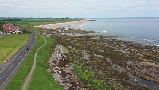Aerial footage of the seaside coastal town of the village of Seahouses, a large village on the North Northumberland coast in England, showing a the road and sandy beach in the summer time.