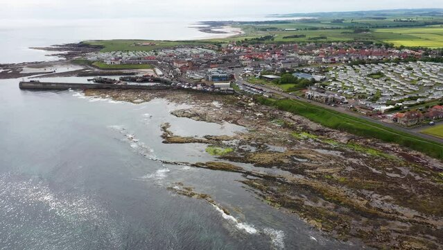 Aerial footage of the seaside coastal town of the village of Seahouses, a large village on the North Northumberland coast in England, showing the harbour and coastal front in the summer time.
