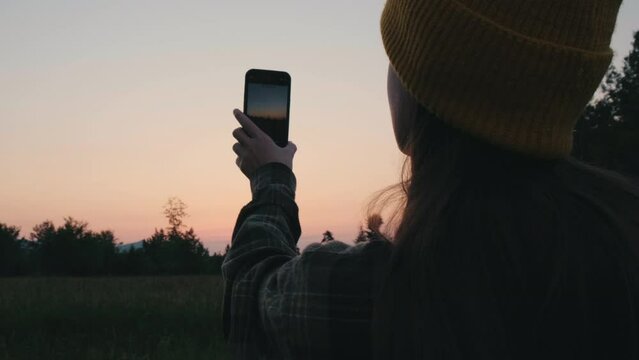 Selective focus of traveler young woman takes pictures at night on smartphone device while standing on background colorful sky. Concept adventure, travel and blogger. Outdoors living lifestyle