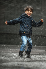 Child walking in wellies in puddle on rainy weather. Boy under rain in summer