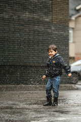 Fototapeta na wymiar Child walking in wellies in puddle on rainy weather. Boy under rain in summer