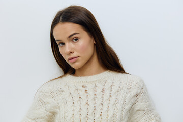 a beautiful, attractive woman in a white autumn, warm sweater stands on a light background looking pleasantly into the camera and smiling gently