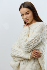 a beautiful, attractive, relaxed woman stands touching her neck with her fingers in a white knitted sweater and gently looks at the camera