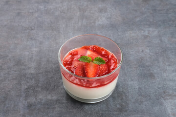 Sweet vanilla silky pudding dessert with strawberry sauce, sliced ​​fresh strawberries and mint on a glass
