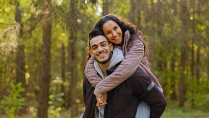 Young hispanic happy couple in love in autumn park handsome guy holding girl on back cute...
